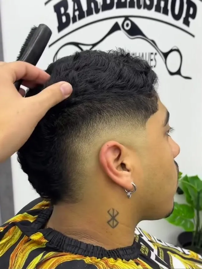 Mohicano con los laterales degradados, visto de perfil, mientras el barbero lo peina