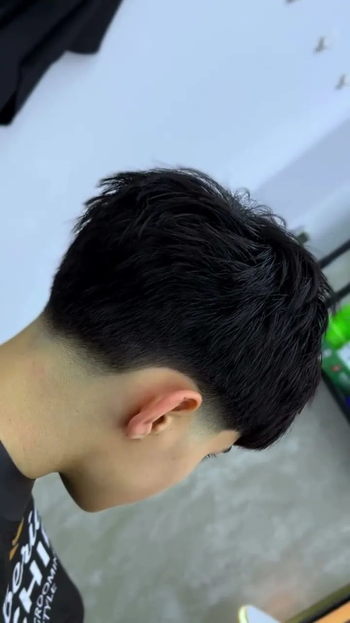 Taper fade visto de espaldas y de lado: degradado bajo en la nuca y detrás de la oreja, con el pelo liso y largo arriba