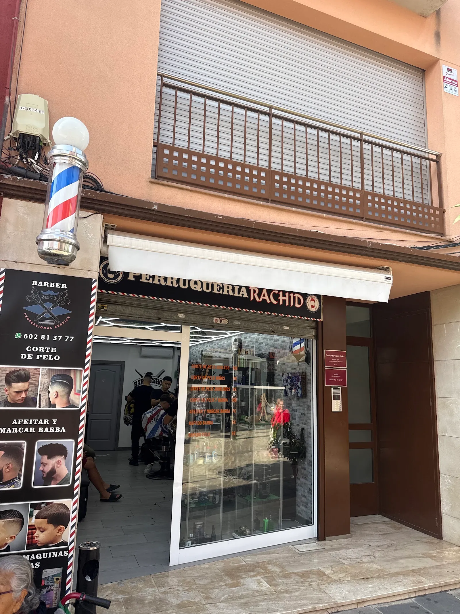 Fachada de la Perruqueria Rachid con el poste de barbero y el rótulo